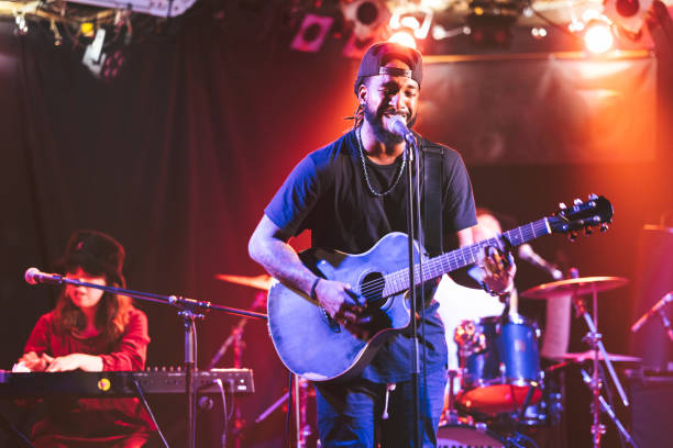 A black male guitarist is singing and playing the acoustic guitar on stage.